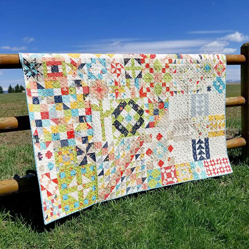 Moda Block Heads 2 quilt at a retreat in Ashton, Idaho | Quiltstock & Restore Quilt Retreats by popular quilting blog, A Quilting Life: image of Moda Block Heads 2 quilt draped over a fence.