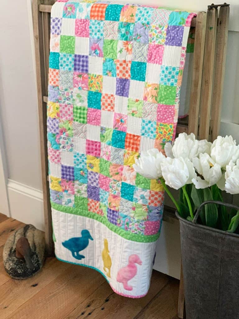 Moda Summer Charm Swap Week 5 by popular quilting blog, A Quilting Life: image of a large pastel block quilt draped over ladder.