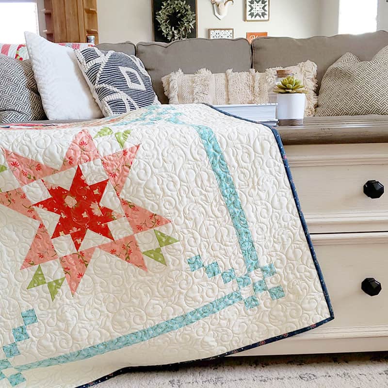 Sunday Best Sampler Quilt by popular quilting blog, A Quilting Life: image of sampler quilt draped over a coffee table.