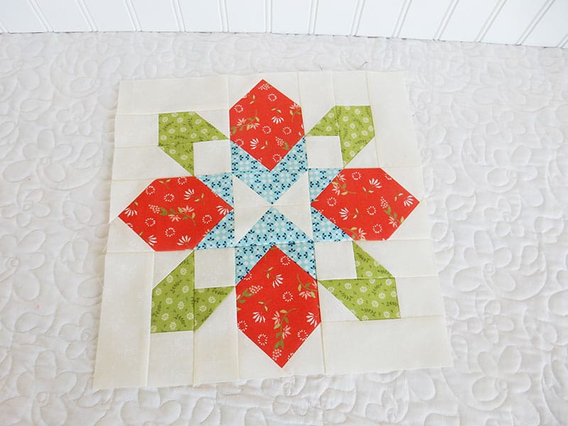 Poinsettia block | Merry Mini Quilt Christmas Quilt Along by popular quilting blog, A Quilting Life: image of red, white, blue and green poinsettia block mini Christmas quilt. 
