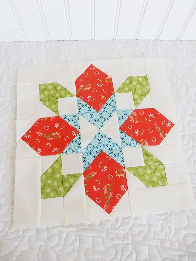 Merry Mini Quilt Christmas Quilt Along by popular quilting blog, A Quilting Life: image of red, white, blue and green poinsettia block mini Christmas quilt. 