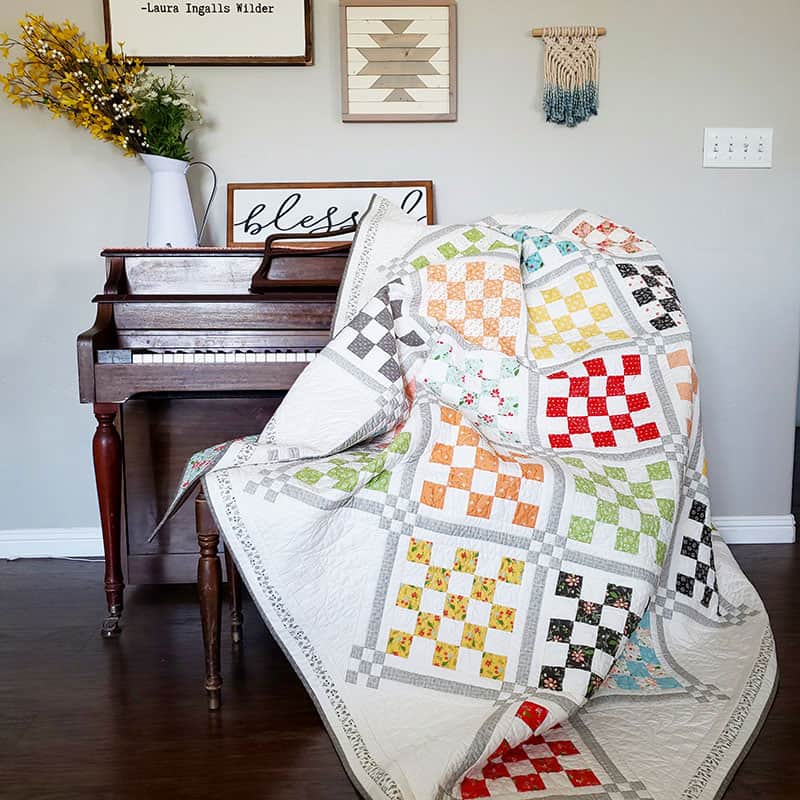 Patchwork Garden 2 | Jelly Roll Quilt Pattern by popular quilting blog, A Quilting Life: image of Patchwork Garden 2 quilt draped over a piano.
