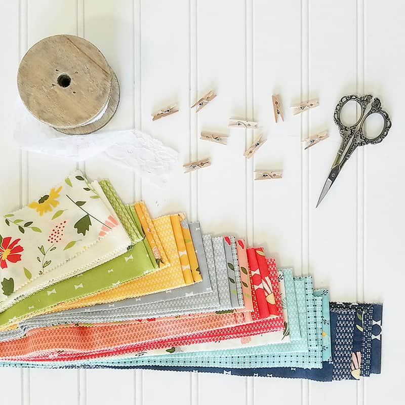 Small Fall Quilt Projects by popular quilting blog, A Quilting Life: image of a pile of Summer Sweet fabric, lace ribbon, sewing scissors, and mini clothes pins. 
