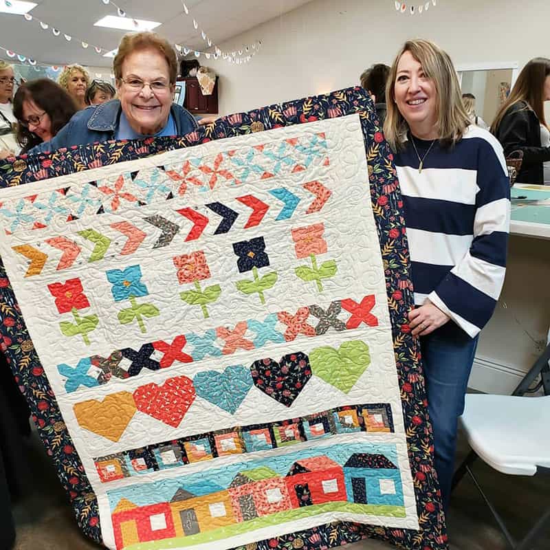  Girlfriend's Day Out Quilt Event by popular Utah quilting blog, A Quilting Life: image of two women standing together and holding up a quilt.