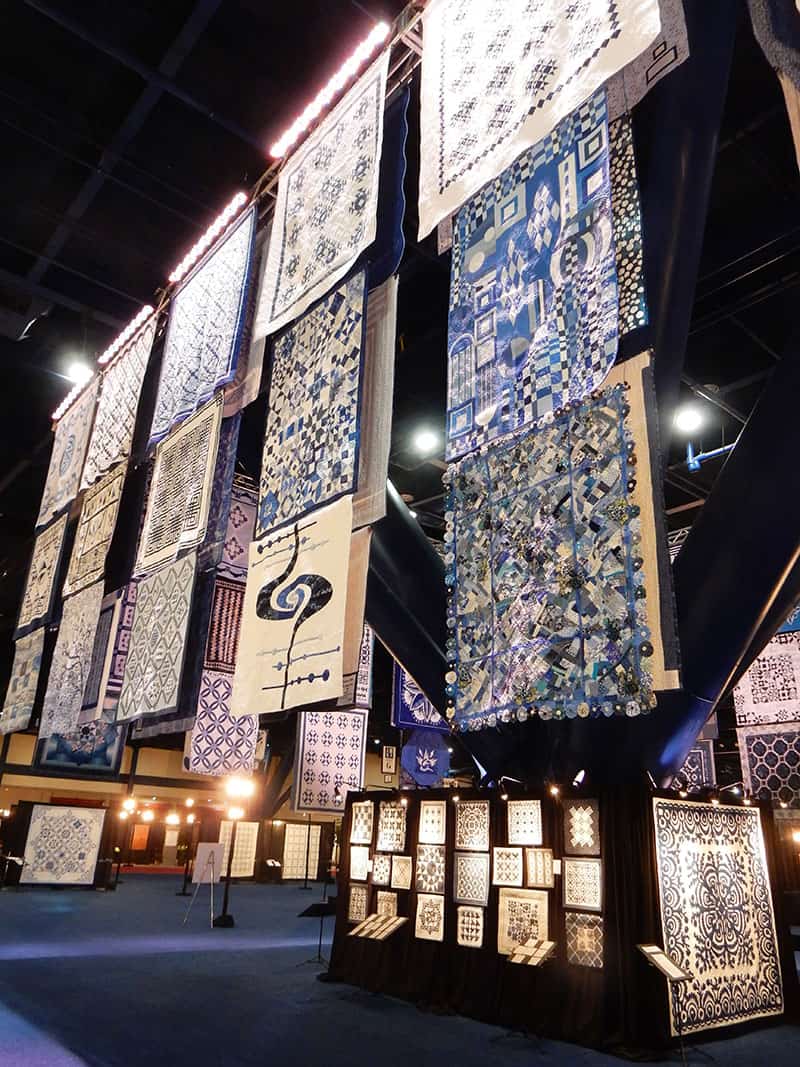 Blue and White quilt display | International Quilt Market Fall 2019: Part 1 by popular Utah quilting blog, A Quilting Life: image of a quilt display hanging from the ceiling. 