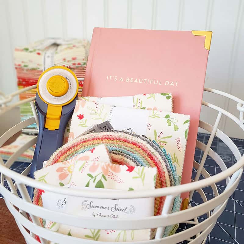 Organizing a Fabric Stash by popular Utah quilting blog, A Quilting Life: image of a rotary cutter, journal, fabric jelly roll, and fabric fat quarters in a white basket.