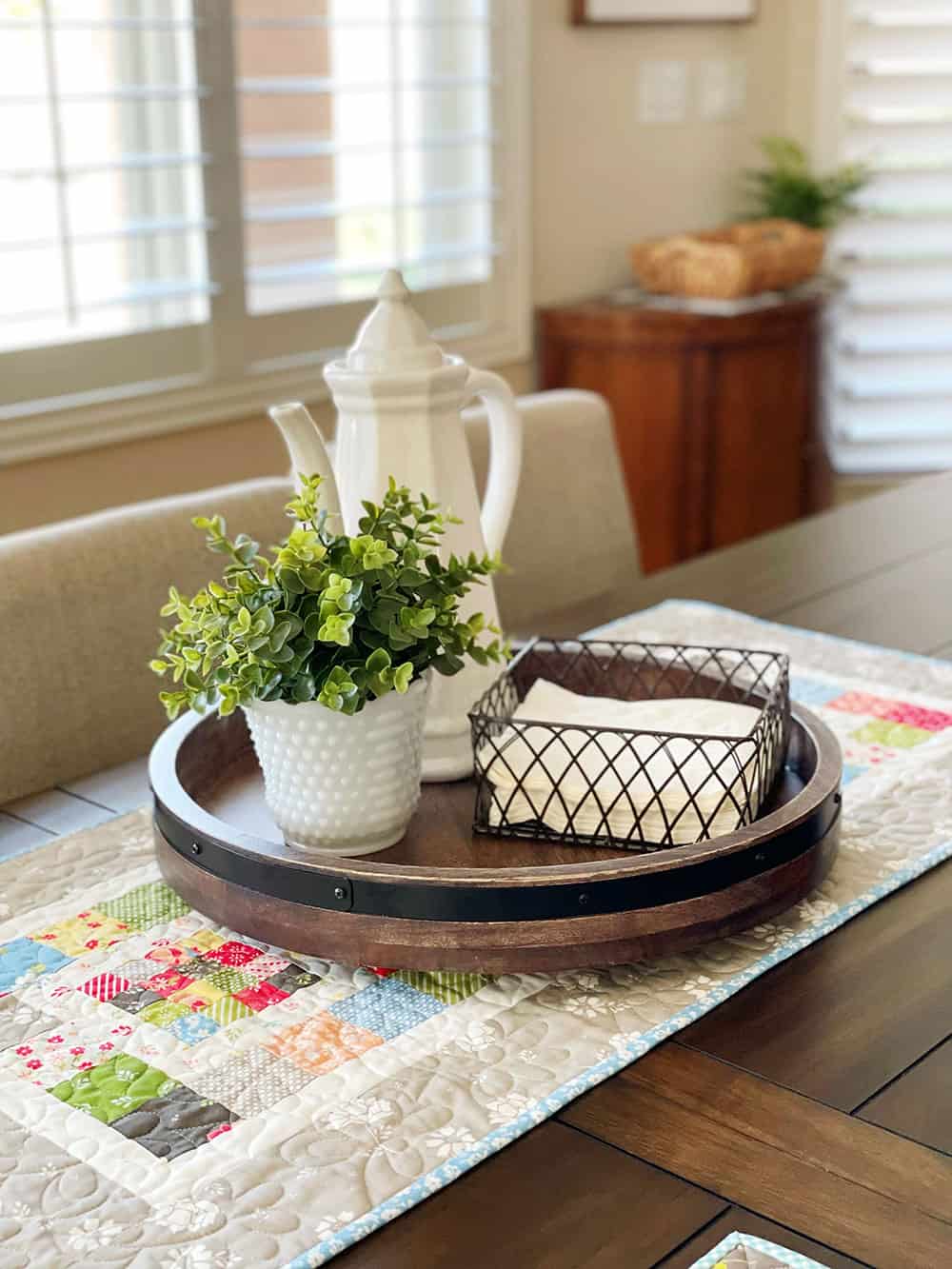 Spring table runner with plant, pitcher, and napkin holder on a lazy susan.