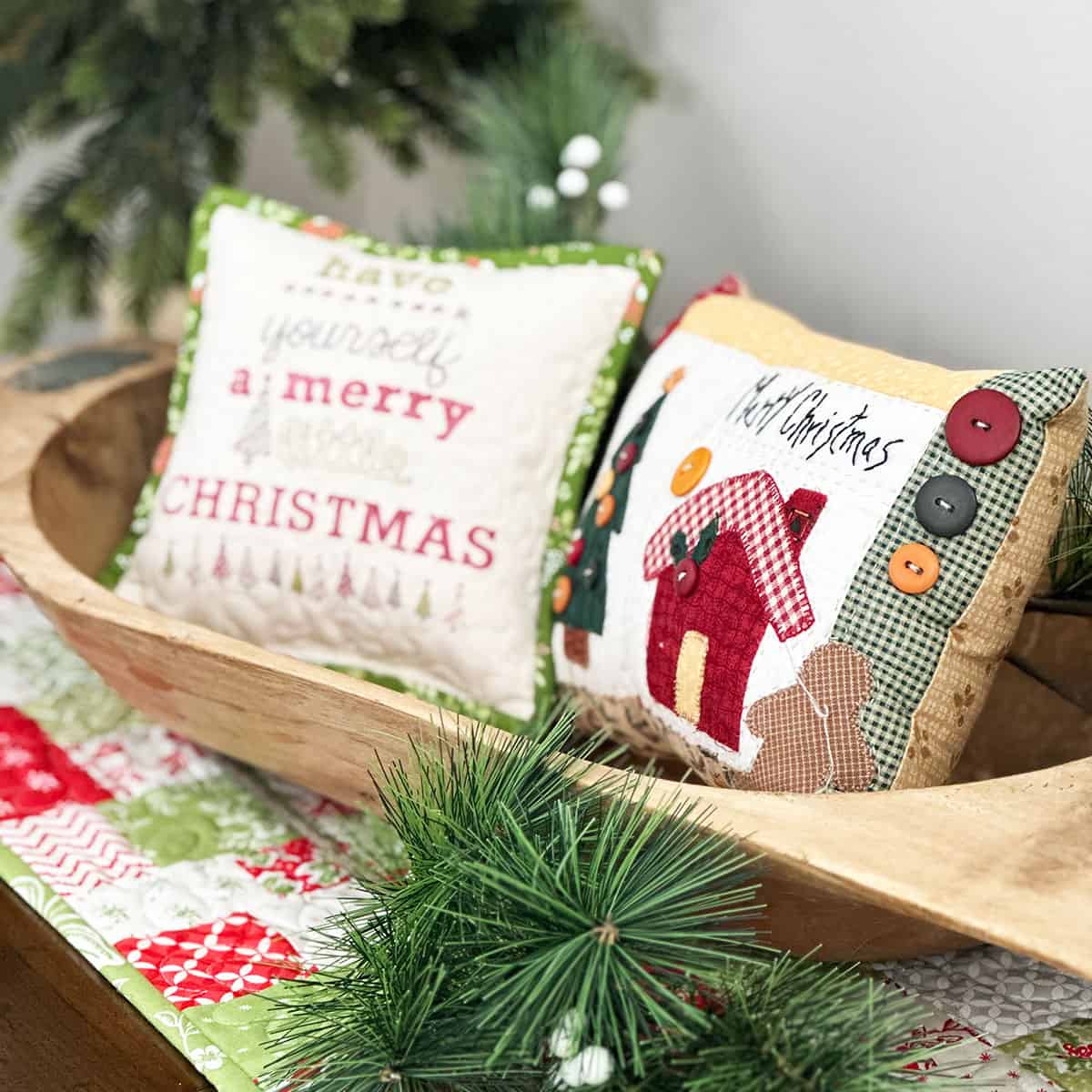 Christmas pillows in a bowl with greenery and table runner