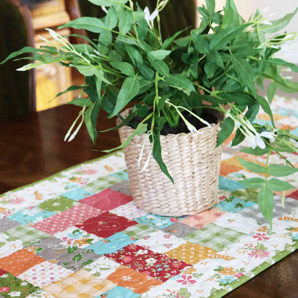 Quilted table runner with plant in wicker basket by Sherri from A Quilting Life