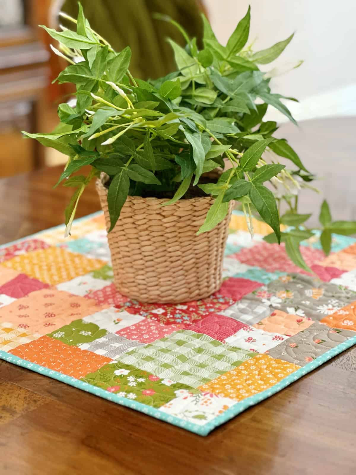 Quilted patchwork table topper with plant on table.