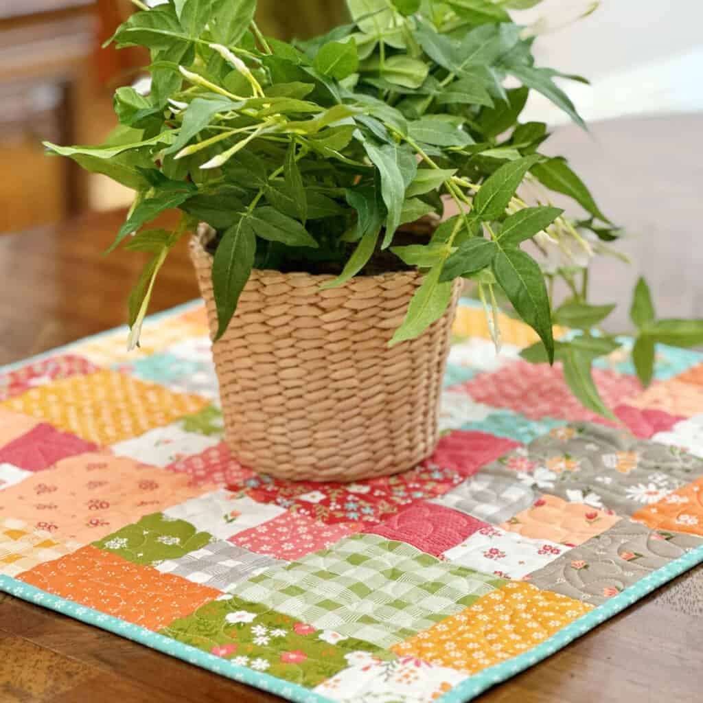 Quilted patchwork table topper in bright fall colors with a potted plant on top.