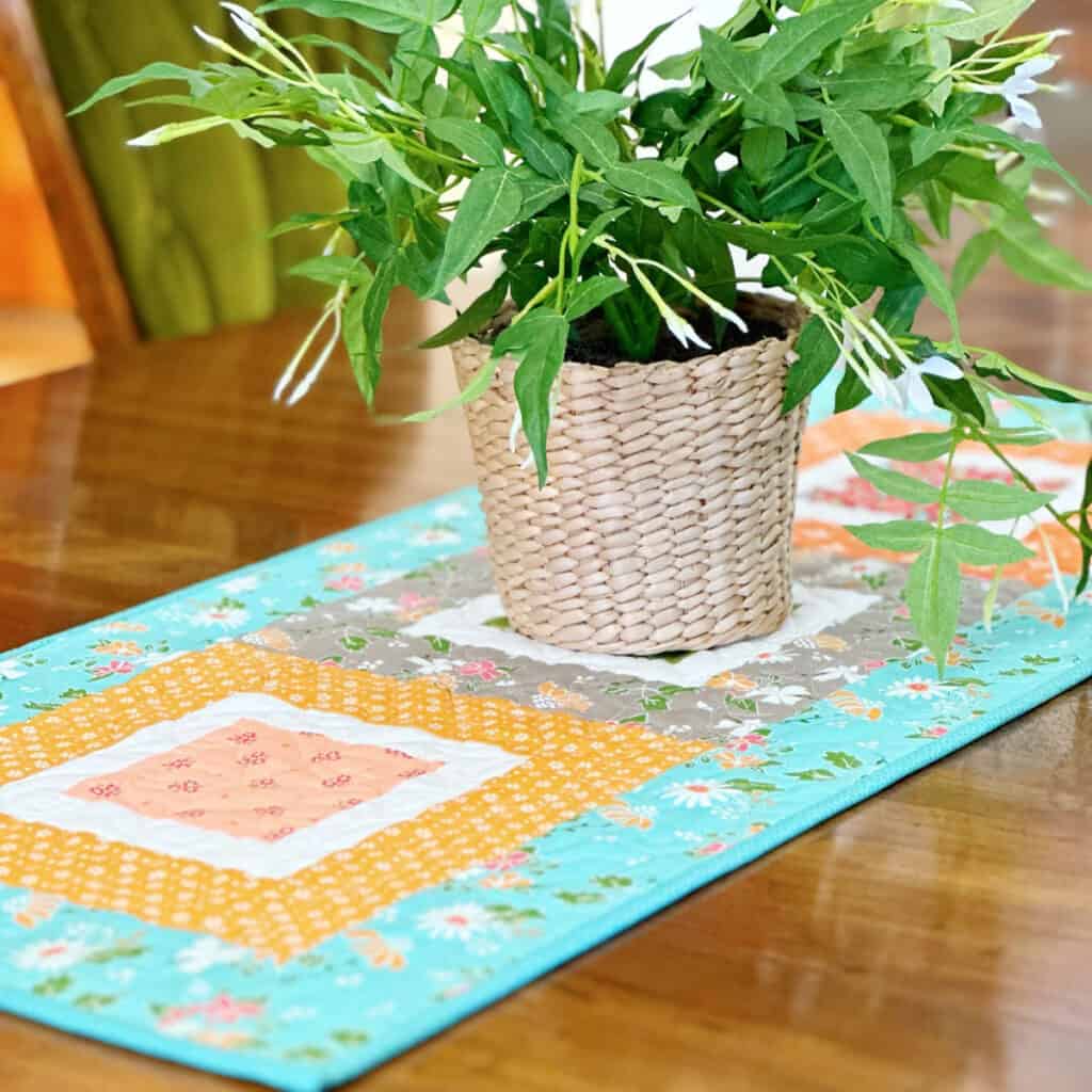 quilted patchwork table runner with potted green plant on table.