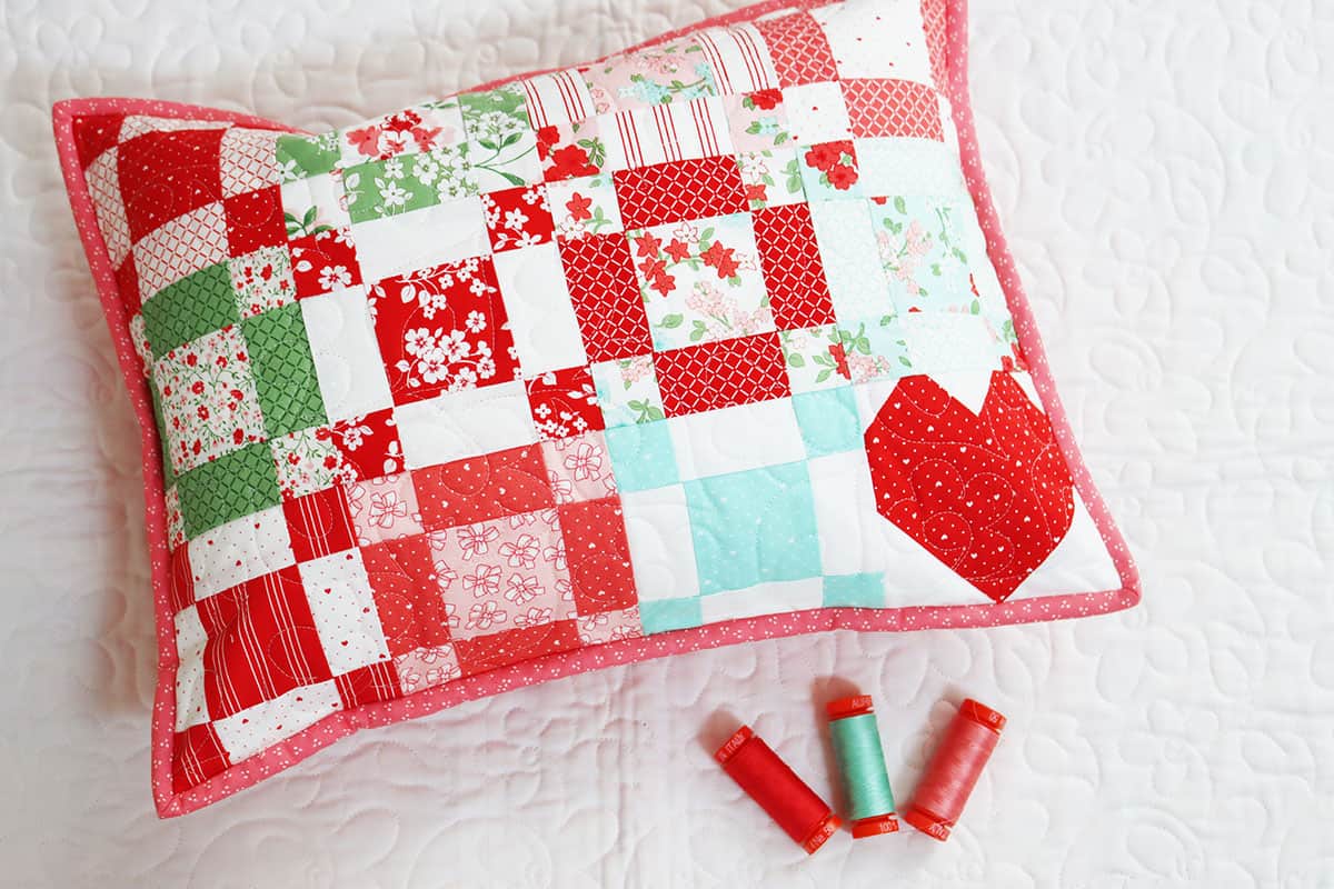 Patchwork pillow with red heart block in lower right hand corner.