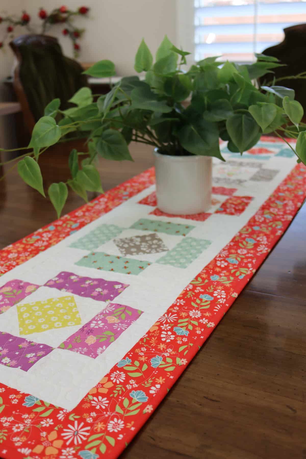Scrappy quilted table runner with plant on top made by Sherri from A Quilting Life