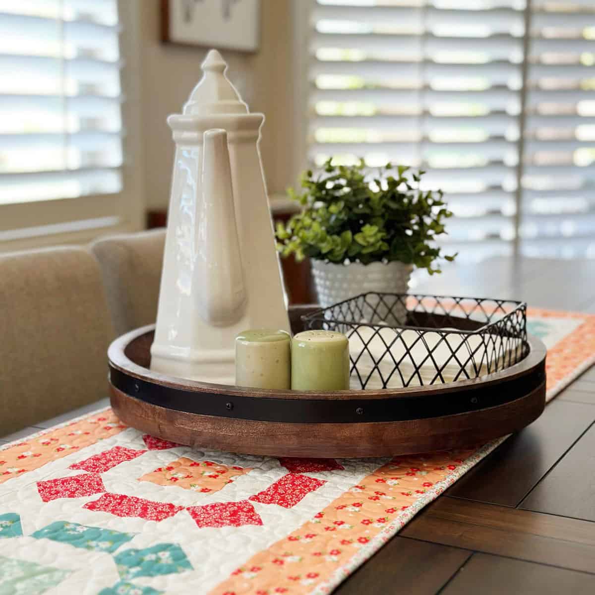 Quilted patchwork table runner with pitcher, floral, and napkins on a kitchen table tray