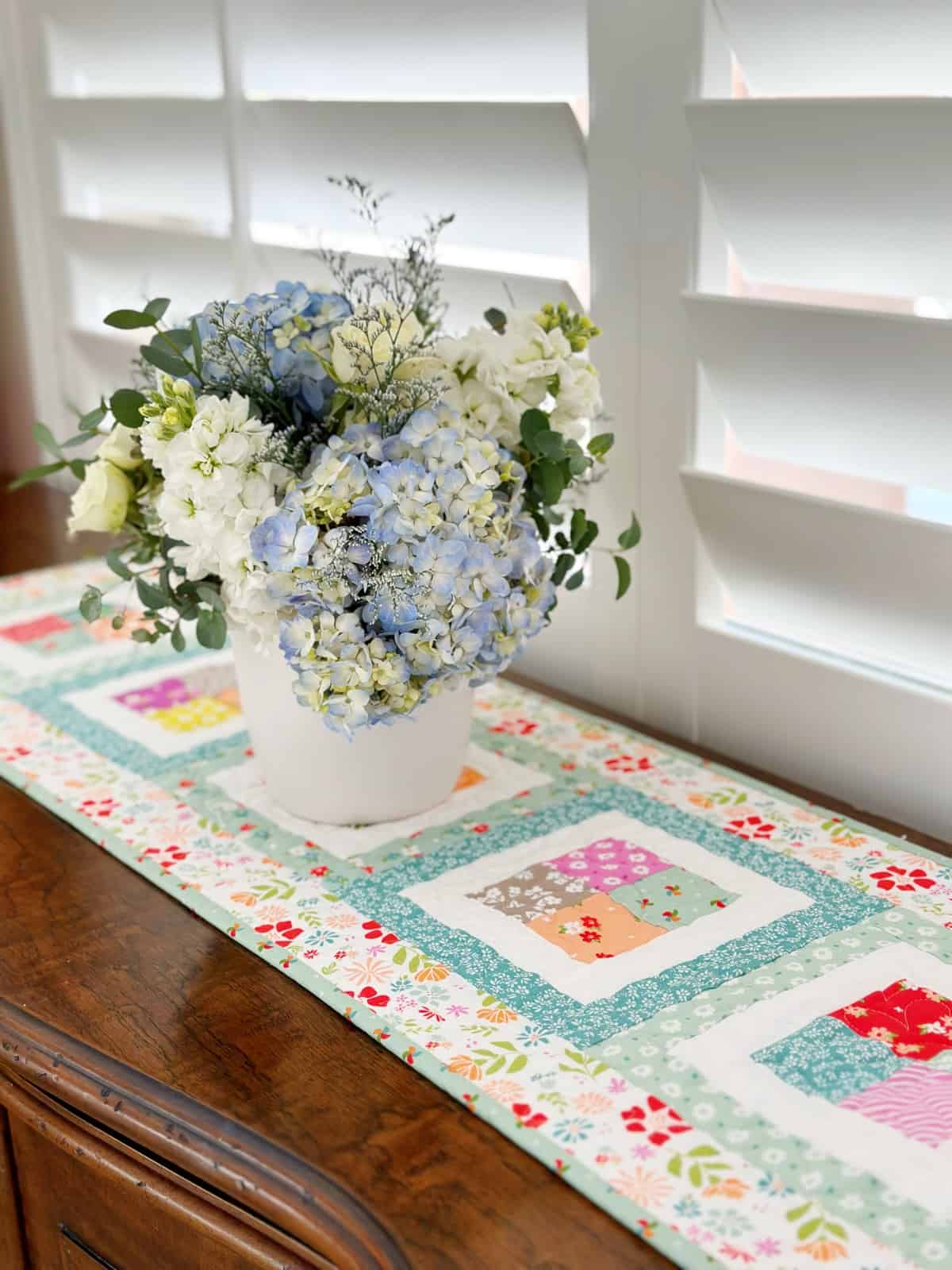 Scrappy patchwork runner in Laguna Sunrise fabrics with hydrangeas in a white bowl.