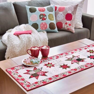 Christmas Table runner and pillows. Used with permission from American Patchwork & Quilting® magazine. ©2025 Meredith Operations Corporation. All rights reserved.